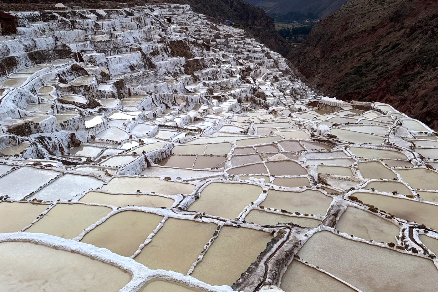 The white salt terraces of Maras stepping down the hillside in narrow pools, with the valley and the peaks beyond