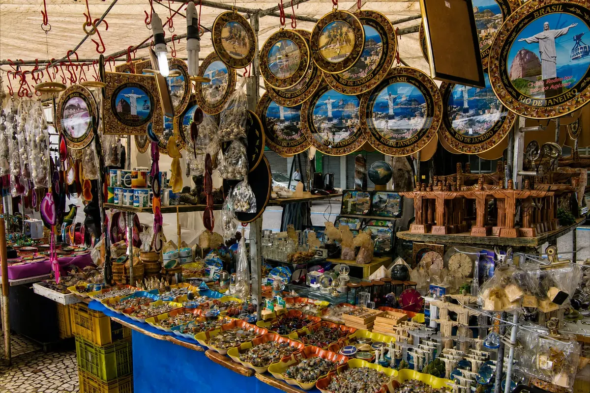 A market stall hung with souvenir plates of Christ the Redeemer over tables of stones, carvings, and keyrings