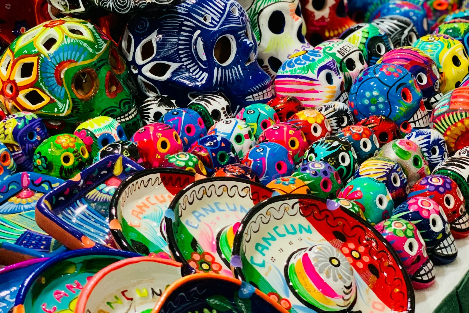 A Cancun market stall stacked with hand-painted ceramic skulls and bowls, several of the bowls lettered Cancun