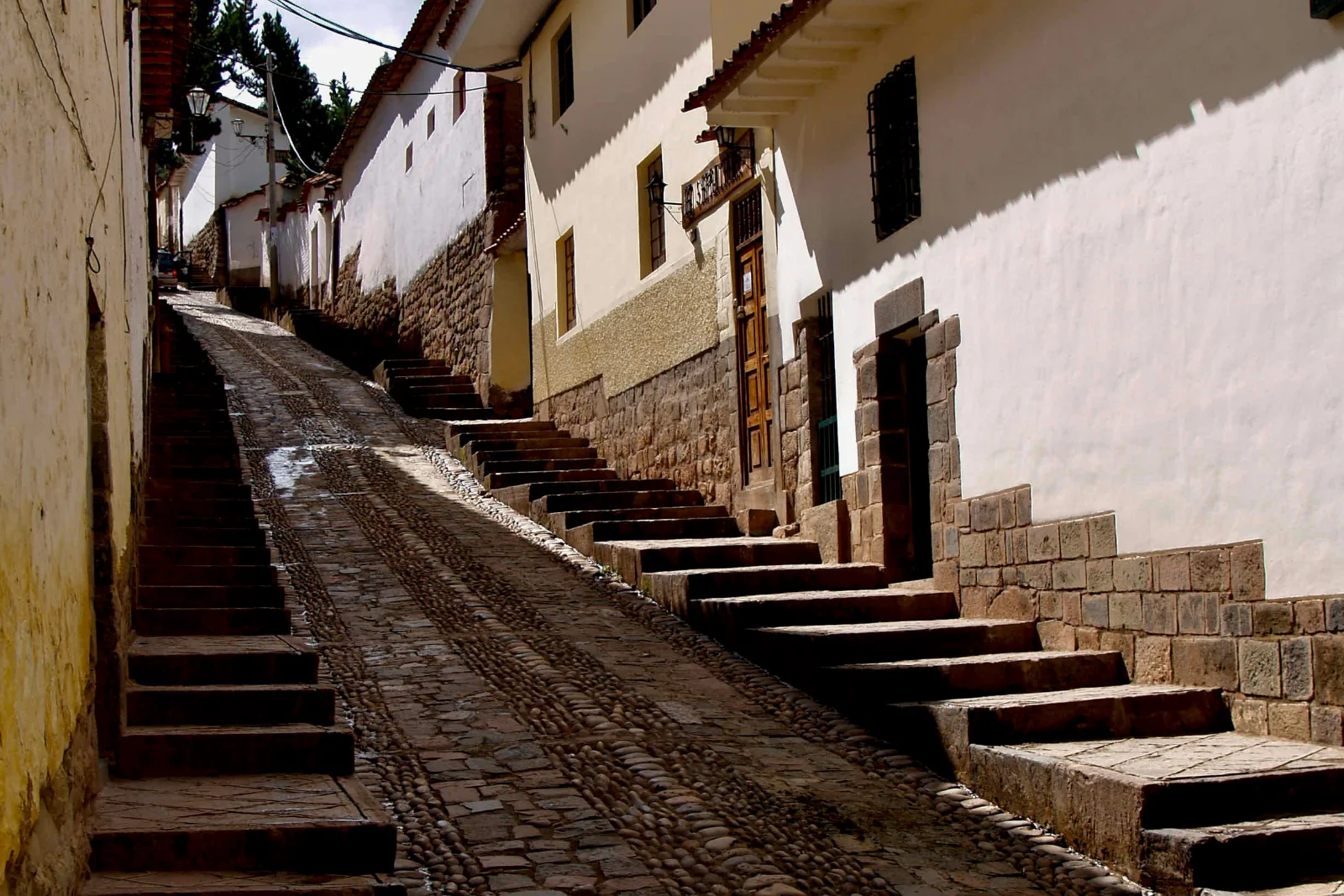 A steep cobbled Cusco lane climbing between stone steps, whitewashed walls standing on Inca stonework