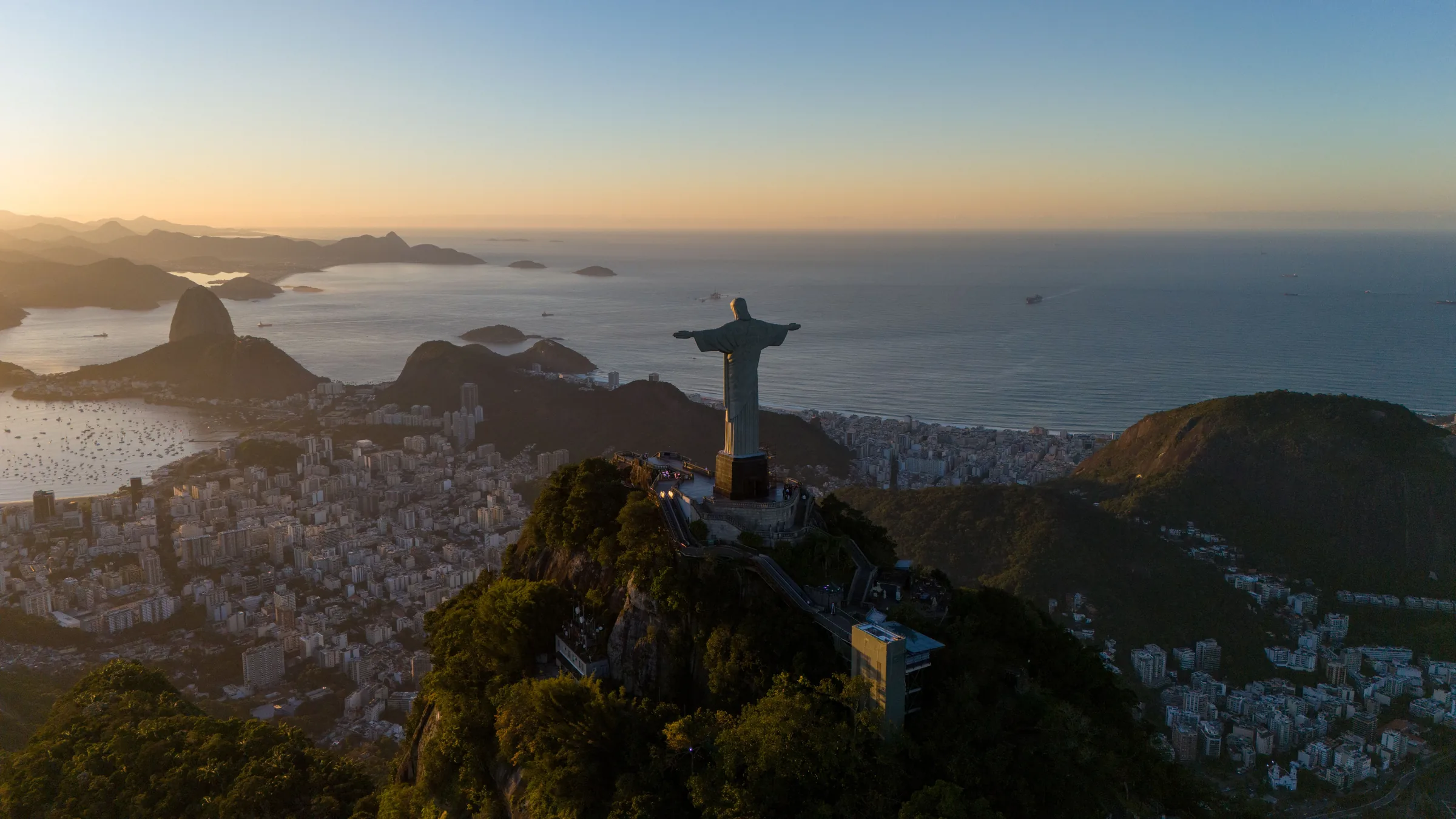 Christ the Redeemer on Corcovado seen from the air in low sun, with Botafogo Bay, Sugarloaf, and the ocean beyond