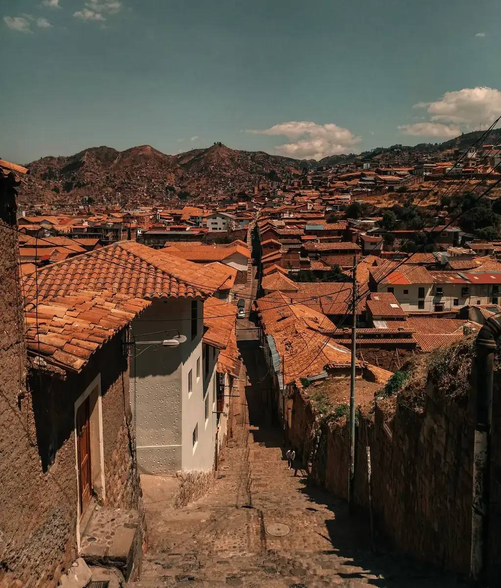A stepped street between tile-roofed houses in Cusco, with hillside neighborhoods beyond