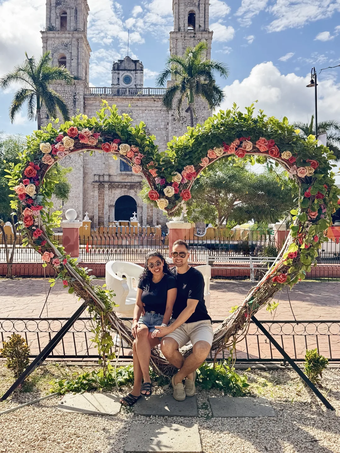 Melissa and Aleksejs under a heart arch of flowers, with a colonial church behind them in Valladolid, Yucatán