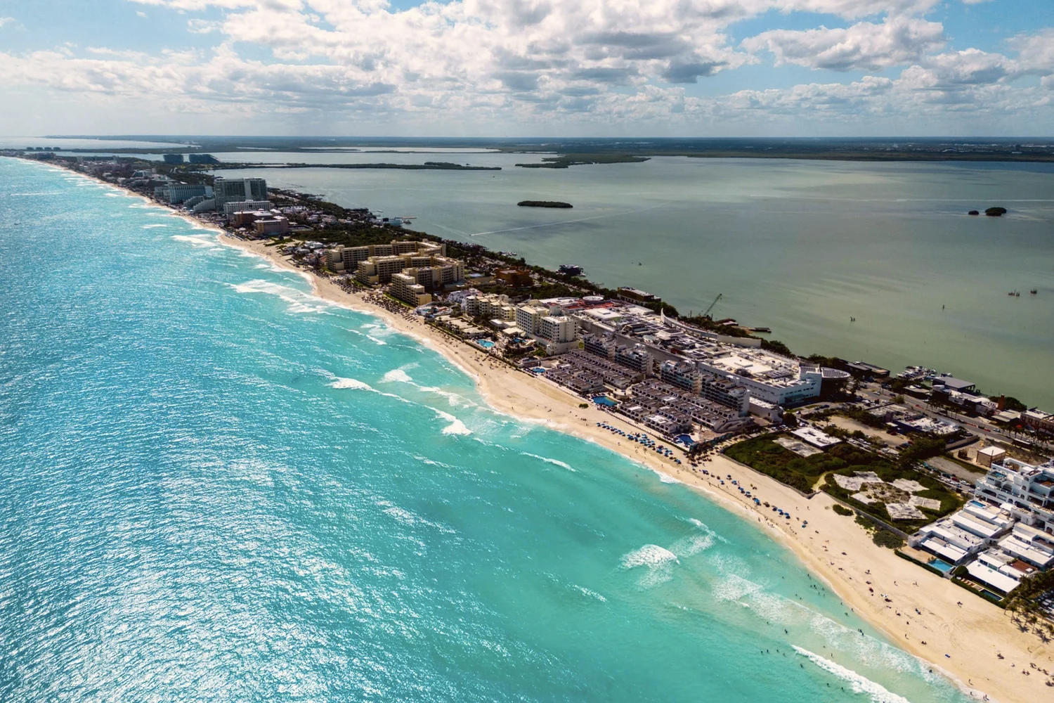 The Cancún Hotel Zone from the air, a narrow strip of hotels and beach between turquoise sea on the left and the lagoon on the right
