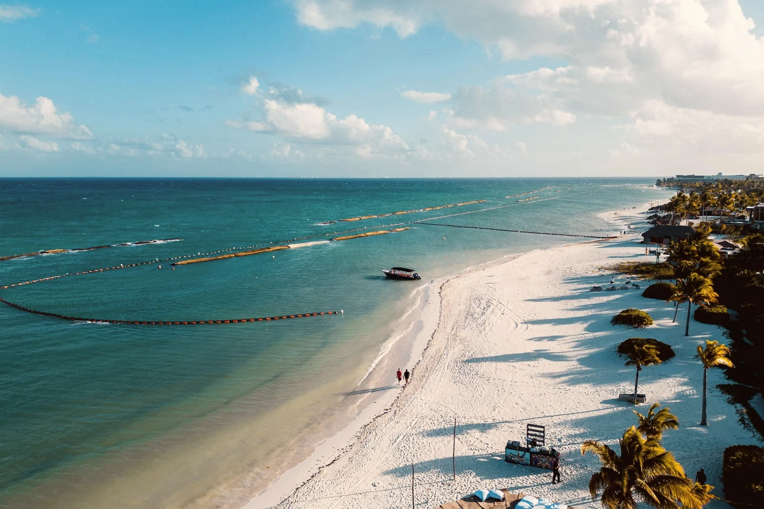 A long white beach at Playa del Carmen from above, palms and loungers on the sand and calm turquoise sea