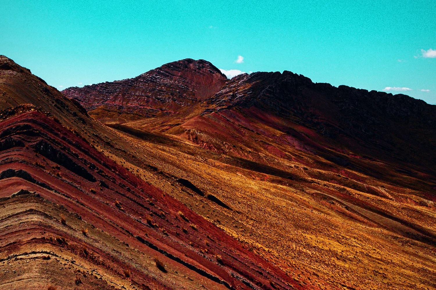The striped red, ochre and green slopes of Rainbow Mountain under a deep blue sky