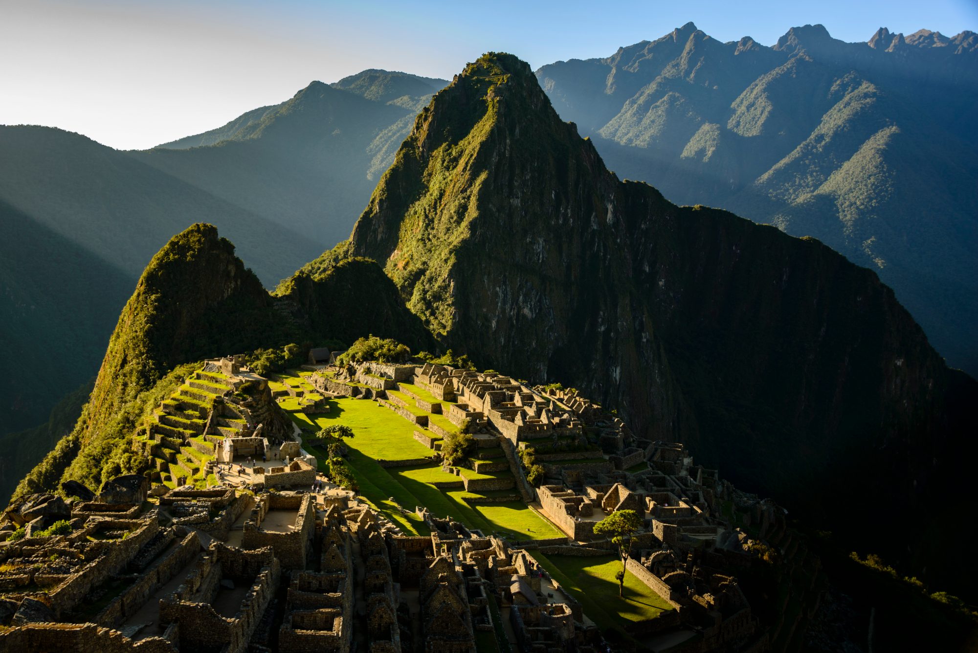First light crossing the terraces and stone houses of Machu Picchu, with Huayna Picchu rising behind
