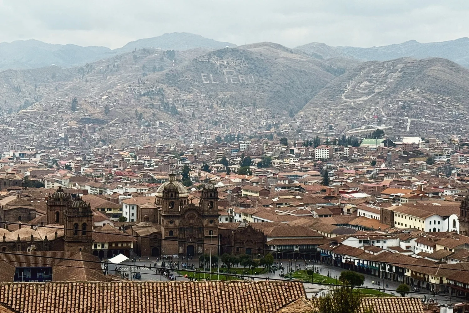 The tiled roofs of Cusco from above, the Plaza de Armas and its churches in the middle and the bare hills behind