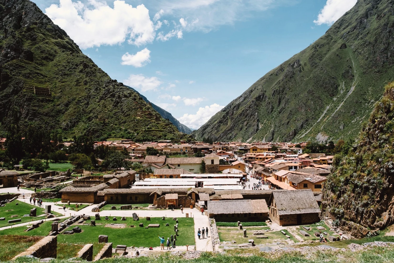 Ollantaytambo below steep green mountains, its roofs and squares spread along the valley floor under a blue sky