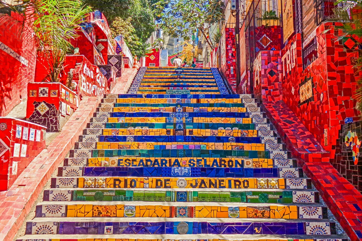 La Escadaria Selarón sube entre paredes pintadas, con cada escalón revestido de azulejos azules, amarillos, verdes y rojos y el nombre de la ciudad incrustado en ellos