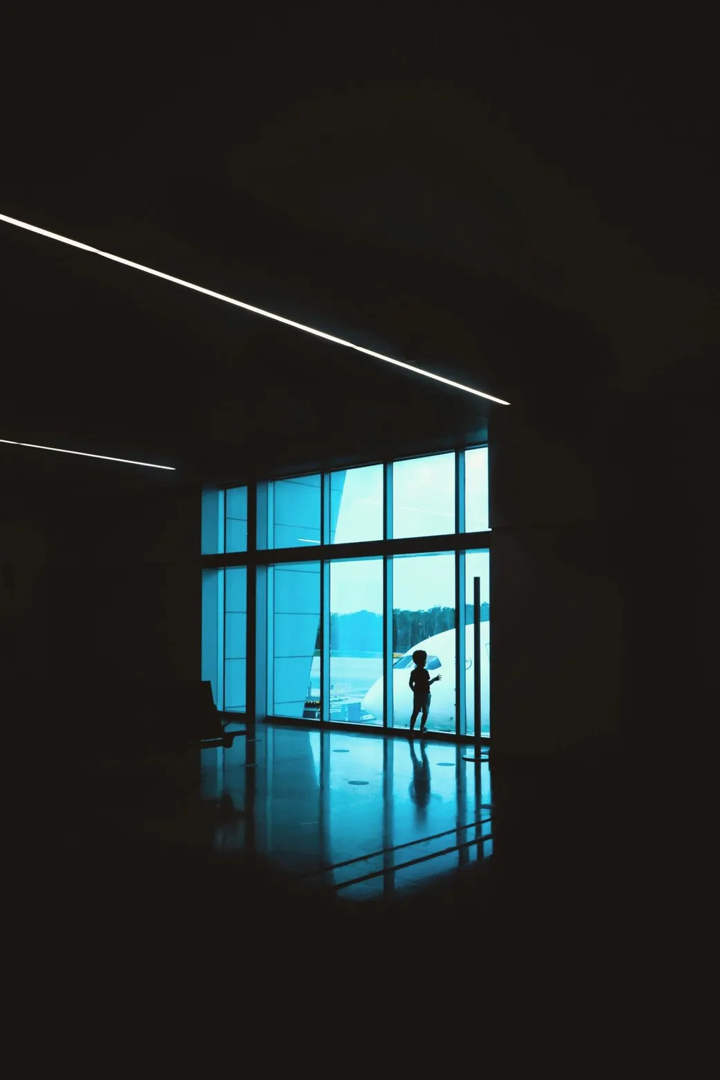 A child at the terminal window, with a plane beyond the glass