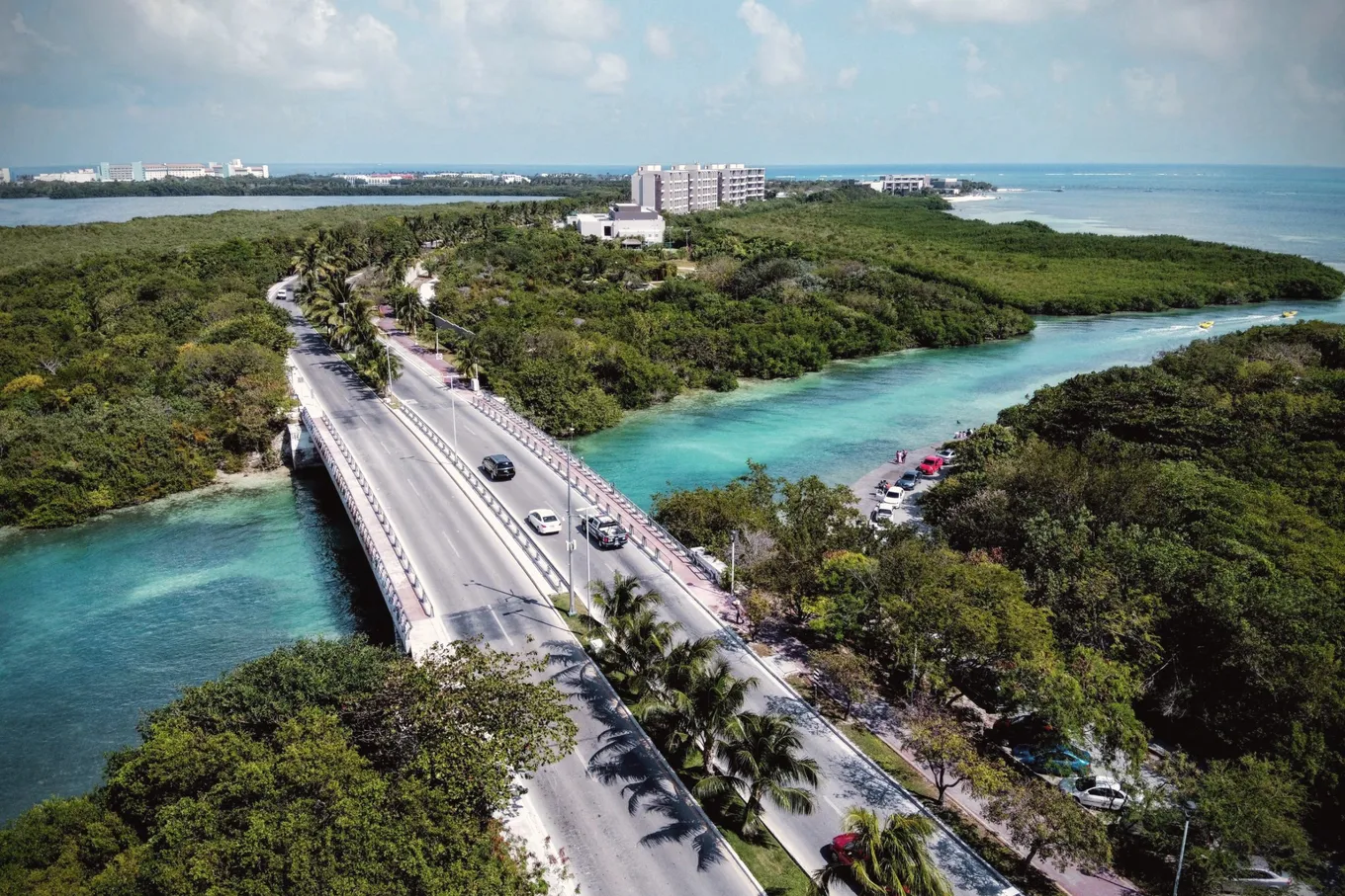 A road and a bridge crossing turquoise lagoon water between mangroves, seen from above