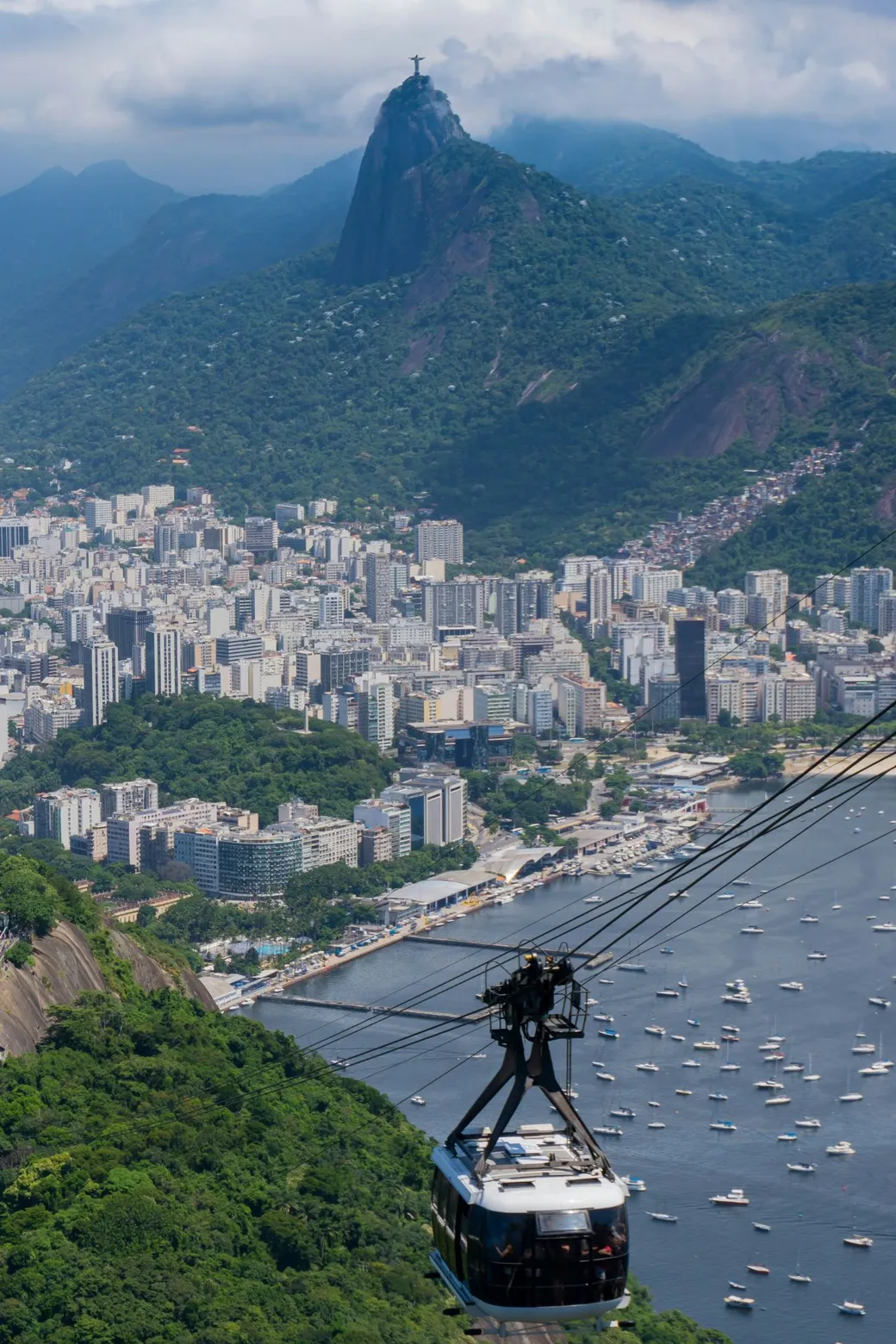 A Sugarloaf cable car over the bay, with Corcovado and the statue far behind it
