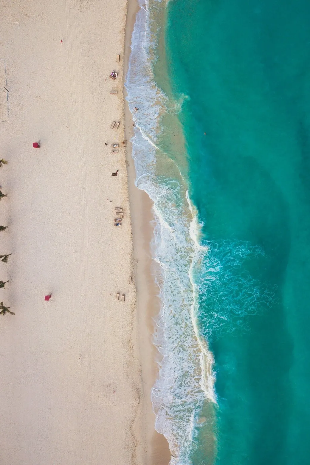 A long beach from above, surf breaking white at its edge