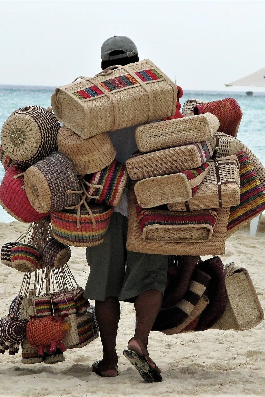 A beach vendor carrying woven baskets and bags