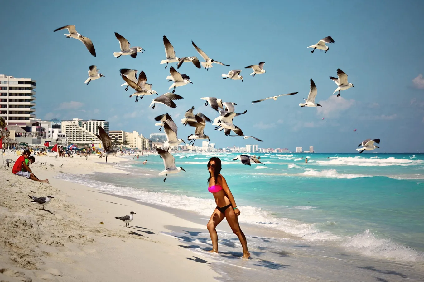 A woman walking through a flock of gulls on a Hotel Zone beach