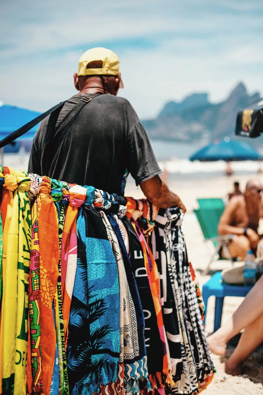 A beach vendor carrying bright sarongs across the sand