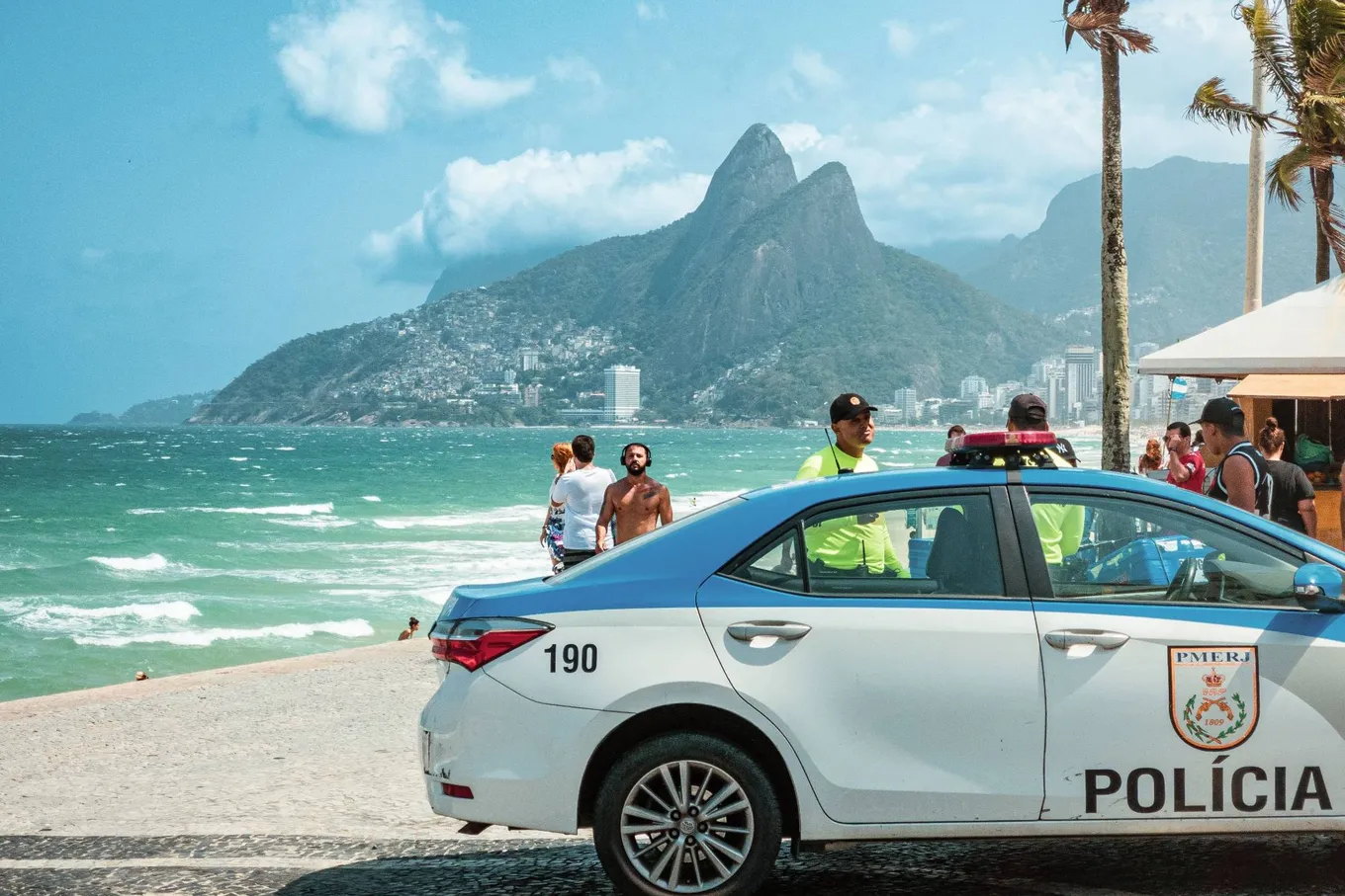 A white and blue police car on the promenade, Dois Irmãos and the sea behind