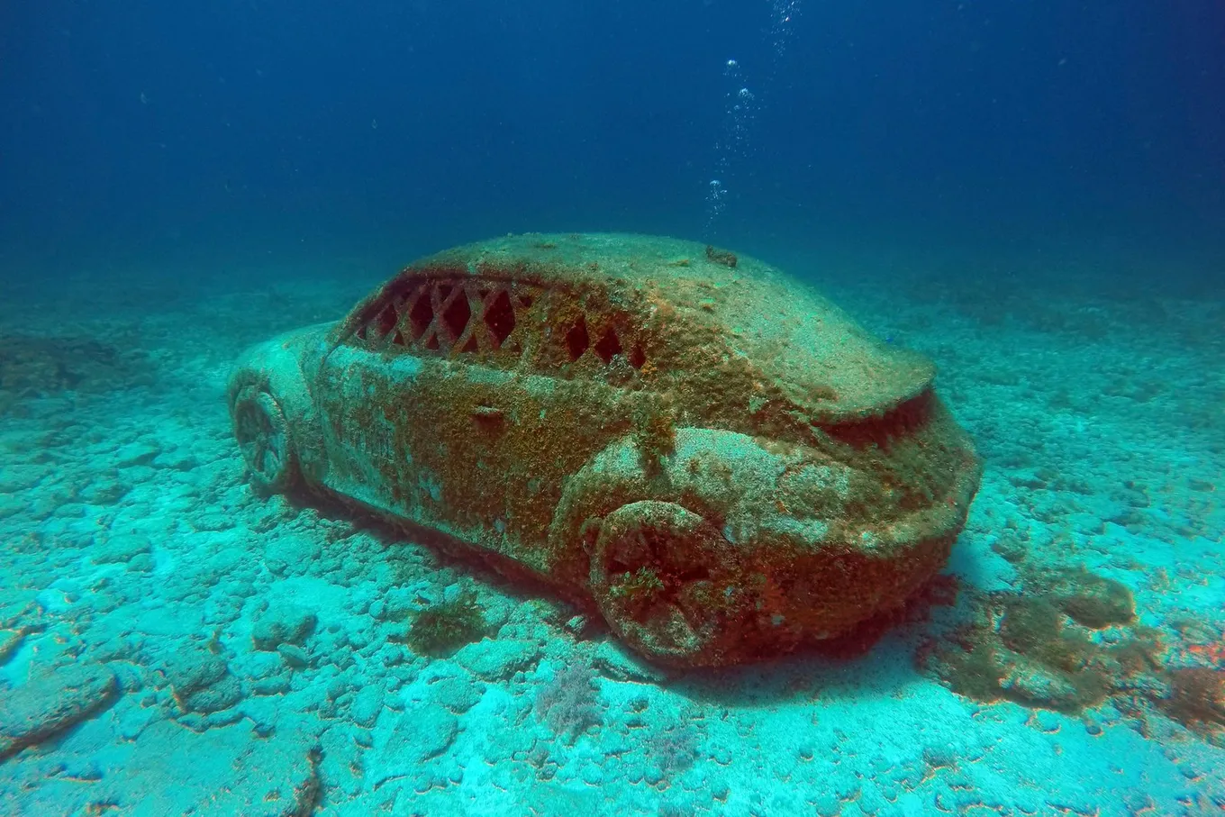 A sculpted Volkswagen Beetle on the seabed, under coral