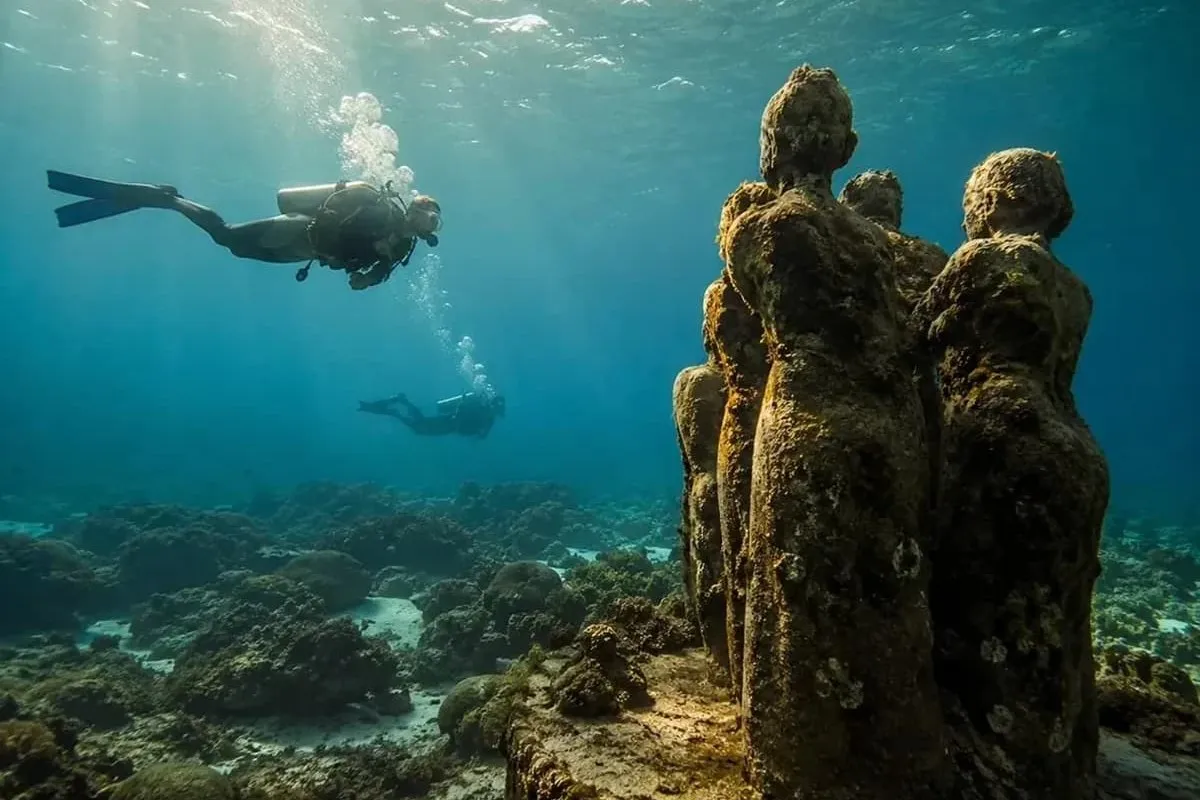 Sculpted figures standing on the seabed, divers passing above