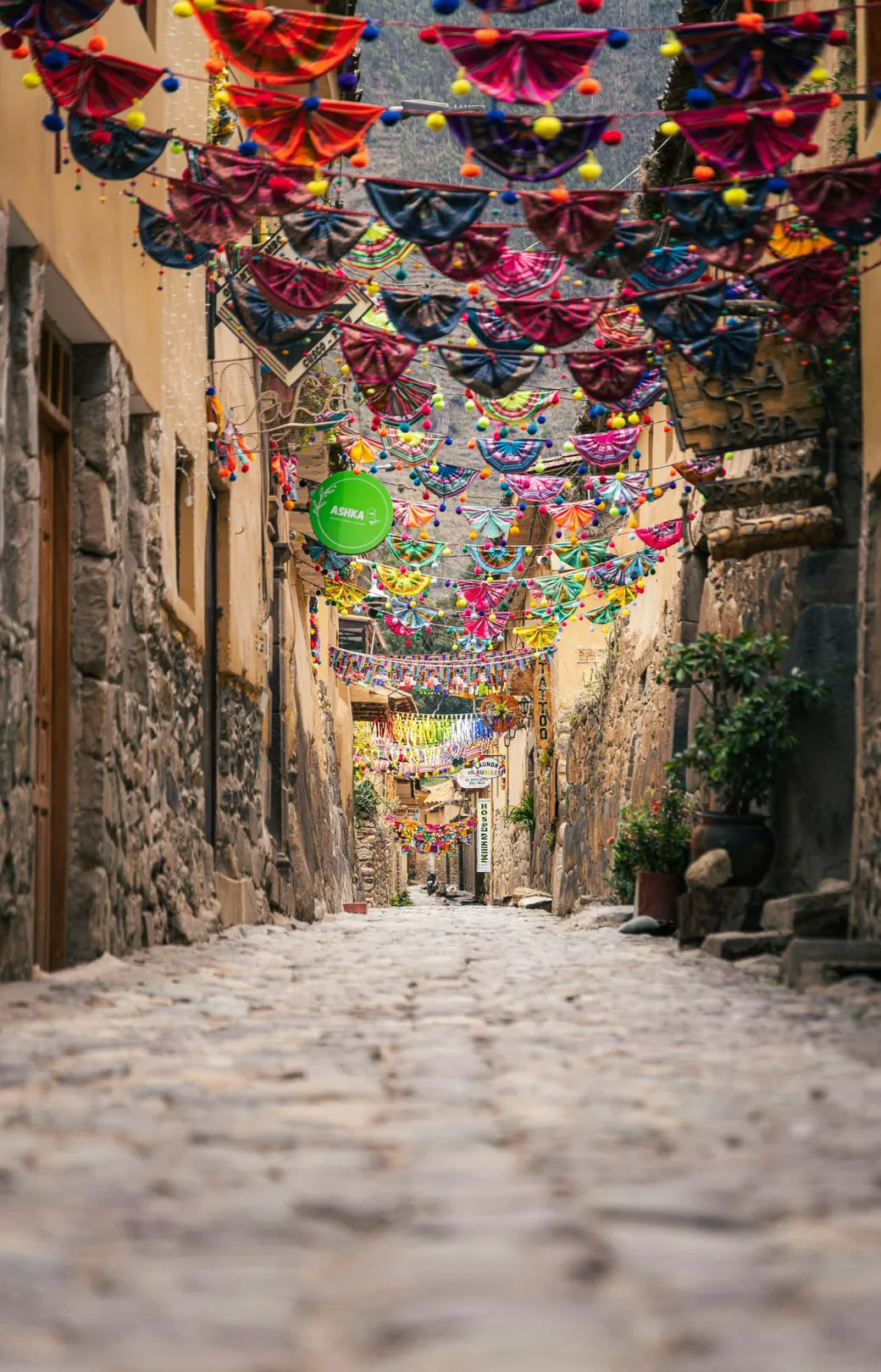 A stone street in Ollantaytambo, under strings of woven bunting
