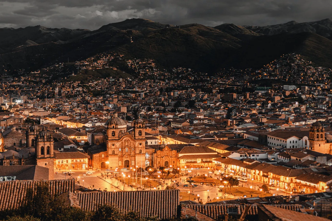 The Plaza de Armas lit at dusk, the hills dark above