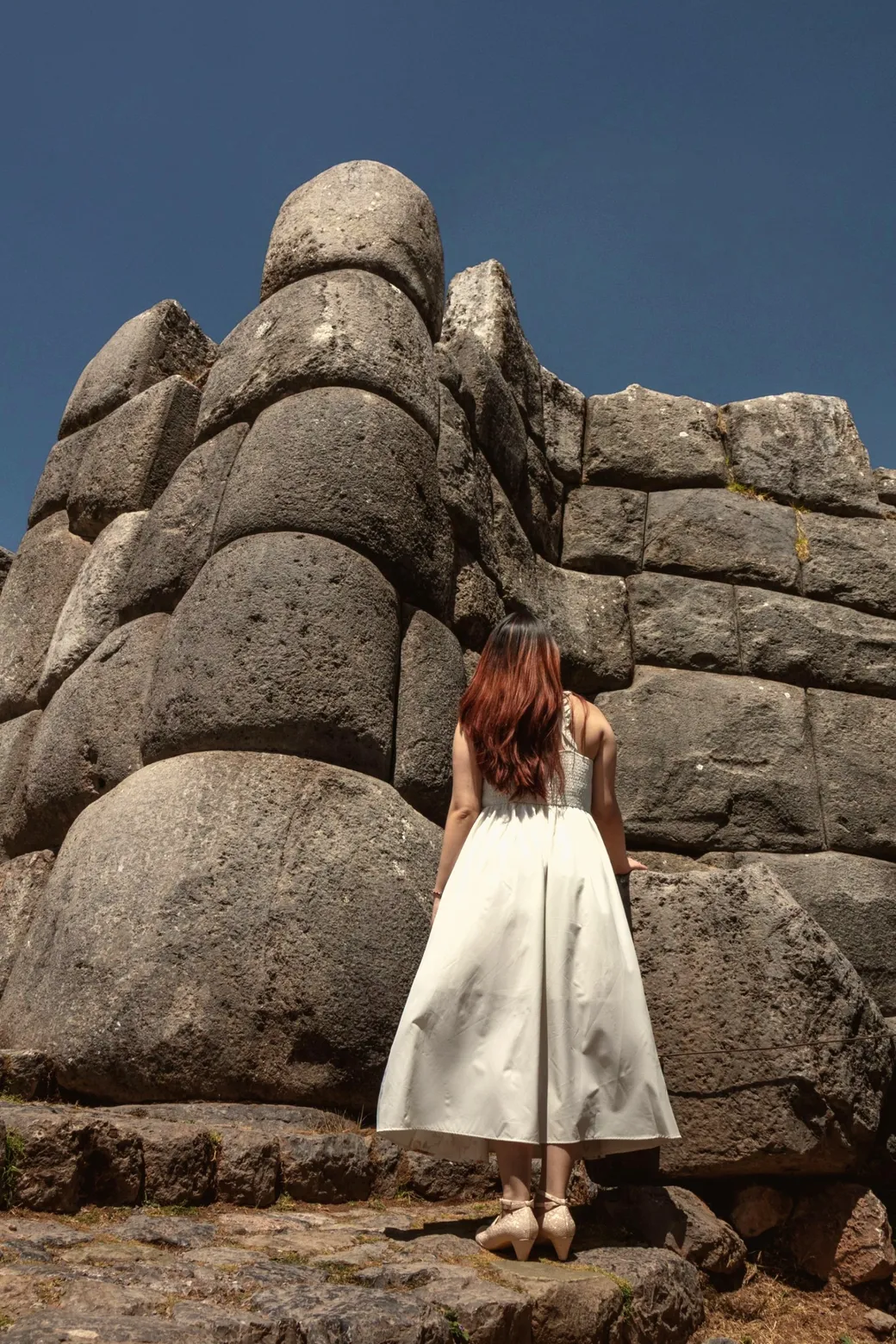 A woman in a white dress at the foot of giant fitted Inca stones