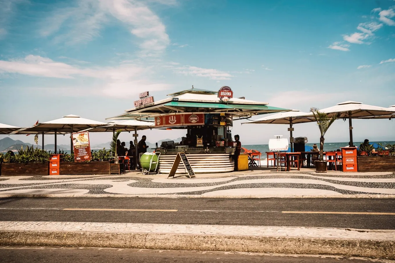 A beach kiosk with a thatched roof and white umbrellas on the Copacabana promenade, the wave mosaic in front