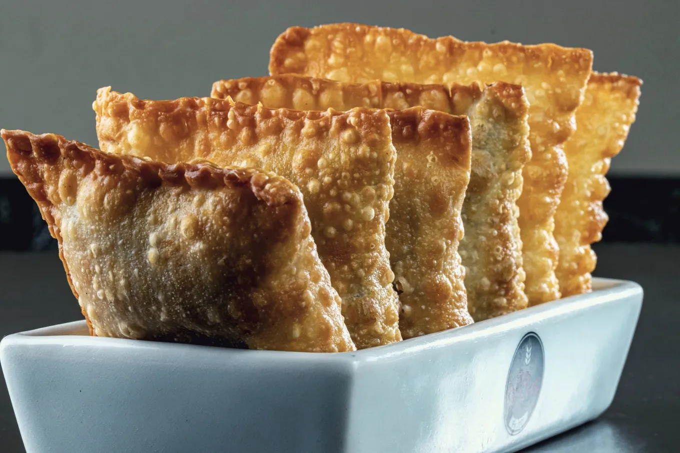 Golden pastéis stacked upright in a white dish
