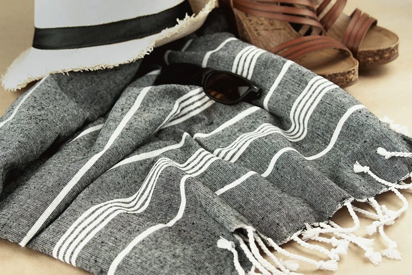 A hat, sunglasses, a striped towel, and leather sandals