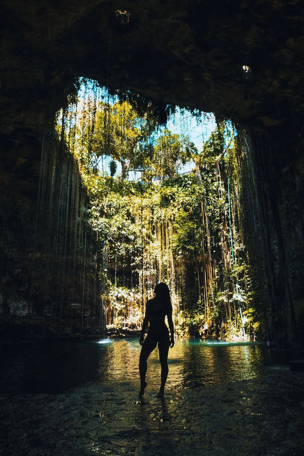 A silhouette in swimwear inside a cenote, below its opening
