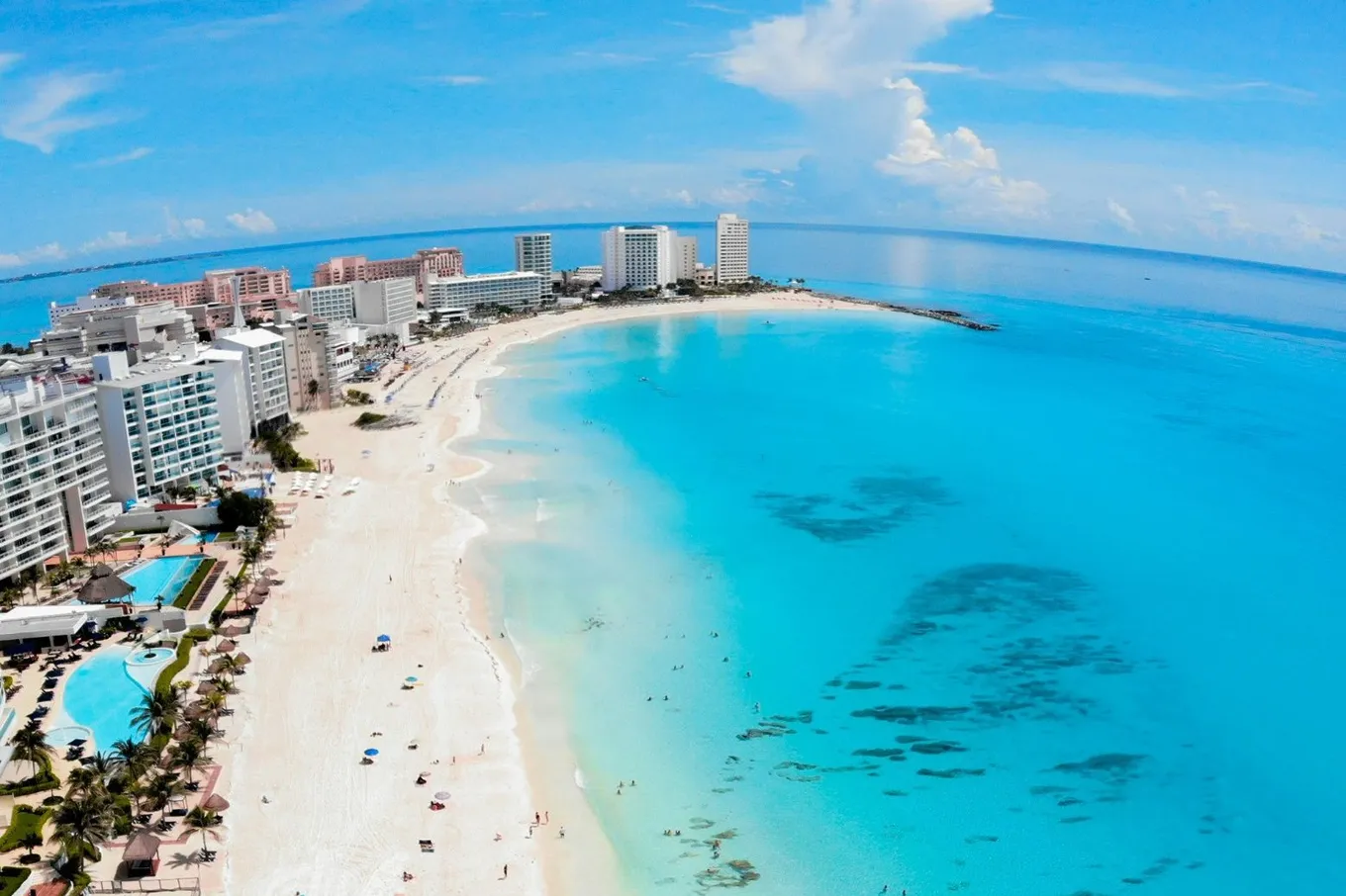 The Hotel Zone from above, hotel towers along a curve of white sand with turquoise shallows and open sea beyond